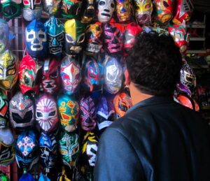 The artist is turned away from the camera, looking at a wall filled with Lucha Libre masks