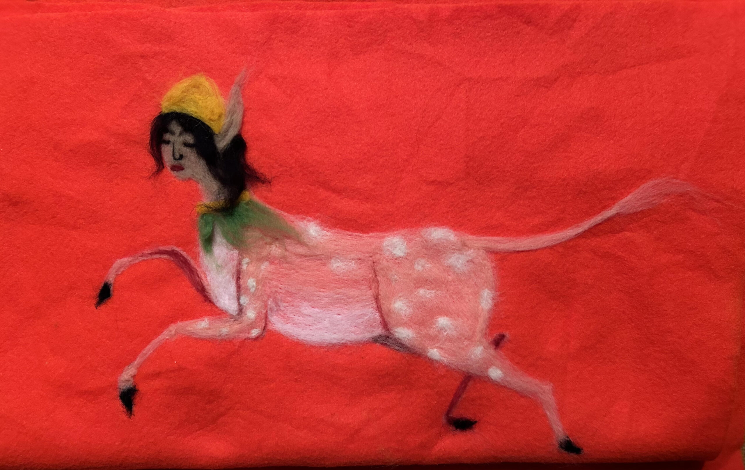 Against a red felt background is a felted figure of a spotted dear-like body with an elf-like head